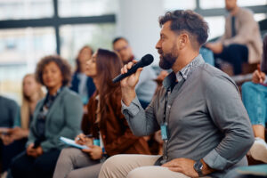 Business seminar attendee talking on microphone while sitting in the audience at convention center.